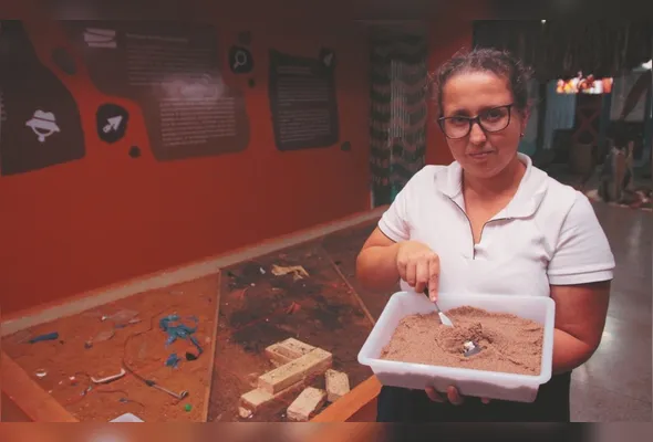 Dionne Azevedo mostra bandeja que os visitantes utilizam para fazer oficinas de  escavação de sítio arqueológico