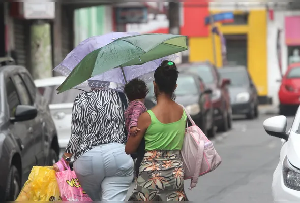 Pedestres se protegem da chuva: previsão inclui também  rajadas de vento e descargas elétricas