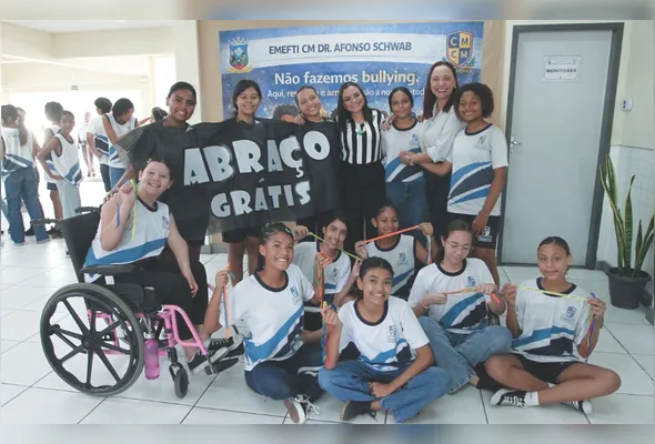 Alunos usam a camisa “Abraço Grátis” e circulam pela escola distribuindo abraços e fitinhas com mensagens positivas para colegas e profissionais