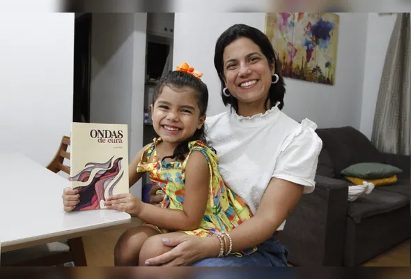 Larissa Belo com a filha Laura no colo e o livro escrito pelo geógrafa