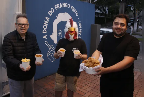 Robson e Dilson, com rosto e delícias do restaurante à mostra, e Gabriel, fantasiado da mascote do restaurante
