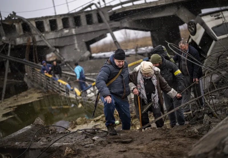Moradores atravessam ponte destruída nos arredores de Kiev, capital da Ucrânia, no 7º dia da invasão russa