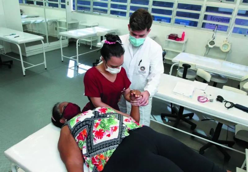 A aluna Barbara Fraga e o professor Osni Stein durante sessão de fisioterapia com a paciente Miriam Rodrigues