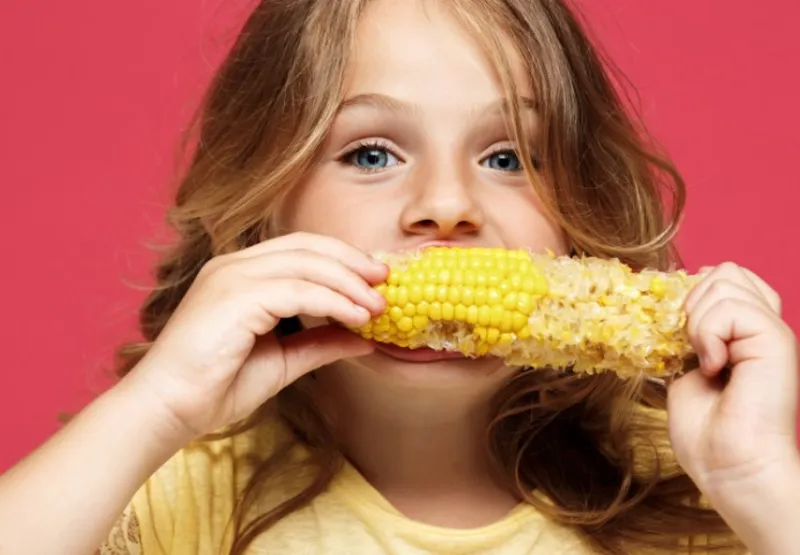 Criança saboreando milho: cereal ajuda no sistema nervoso e hormonal e contribui para aumentar a imunidade