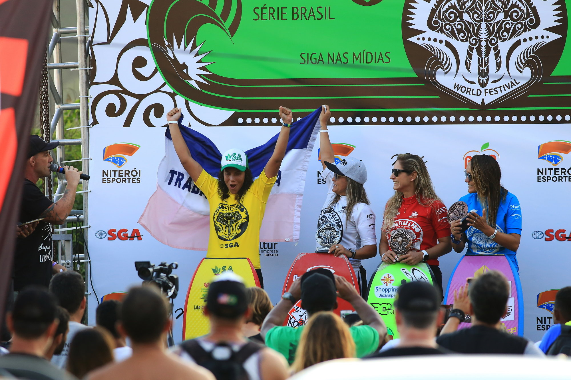 Maira Viana vibra no pódio com a bandeira do Espírito Santo, observada pelas capixabas Neymara Carvalho e Maylla Venturin (Foto: Tony D´Andrea/Itacoatiara Pro)