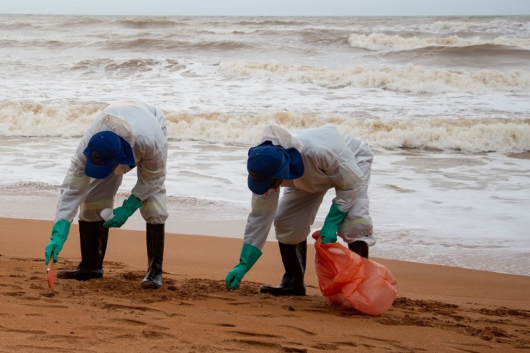 Funcionários da prefeitura realizam a coleta de óleo encontrado na praia (Foto: Divulgação/Prefeitura da Serra)