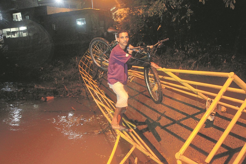 Morador carrega a bicicleta para conseguir atravessar o que restou da ponte (Foto: Dayana Souza/AT)