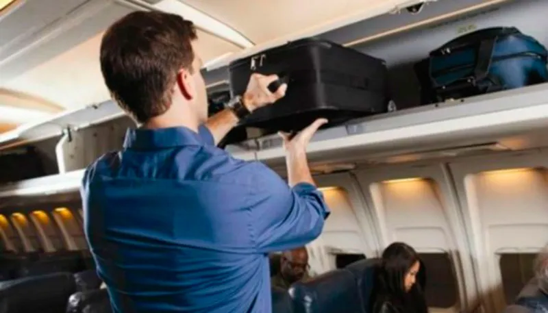 Passageiro acomoda bagagem de mão em compartimento dentro do avião