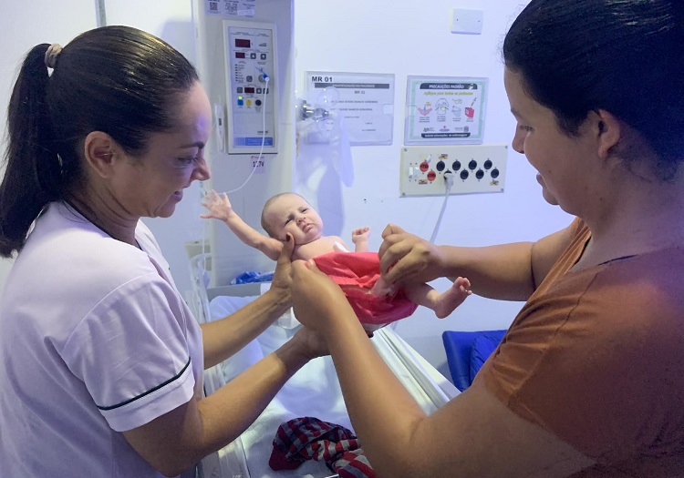 Mãe veste roupa na filha com ajuda de funcionária do hospital. Bebê ficou dois meses com sexo indefinido. (Foto: Divulgação/SESA)