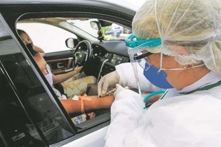 Profissional tira sangue de paciente em sistema de drive-thru para realizar exame que detecta vírus