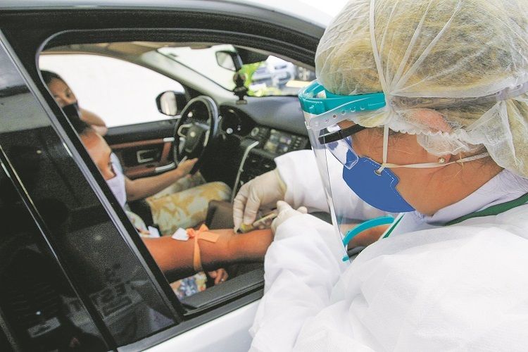 Profissional tira sangue de paciente em sistema de drive-thru para realizar exame que detecta vírus (Foto: Dayana Souza/AT)