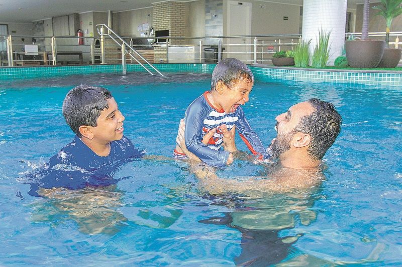 O síndico Gilmar Assumpção com os filhos na piscina de edifício em Vila Velha: regra prevê uso por pessoa ou família (Foto: Dayana Souza/AT)