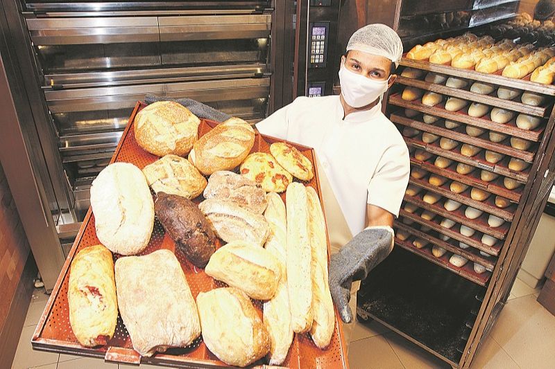 O padeiro Vinicius Dantas Januário mostra os vários tipos de pães feitos em estabelecimento (Foto: Beto Morais/ AT)