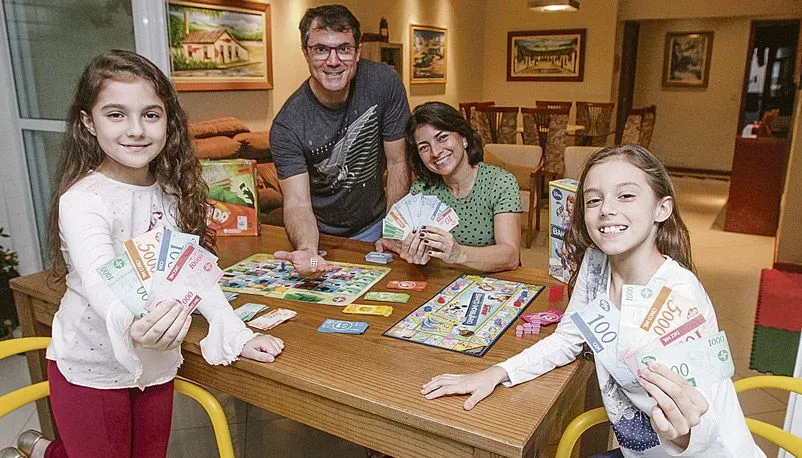 Alexandre, Karla e as filhas Manuela e Isabela brincam de jogo que simula um mercado imobiliário