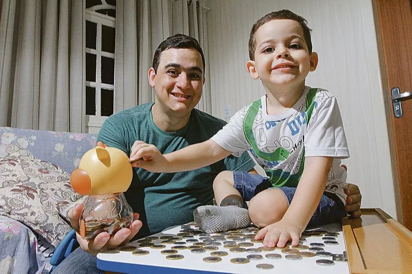 Fabrício Nunes ensina o filho, Roger, a juntar moedas em um cofrinho para poder comprar um carrinho elétrico