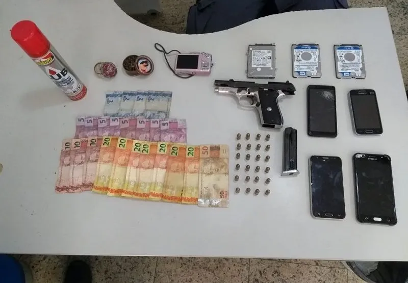 Pistola, munição, celulares, dinheiro e outros objetos apreendidos na casa de Kelvin da Silva.