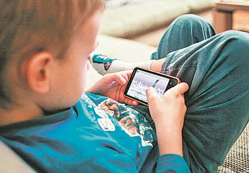 Criança usa smartphone em posição inadequada: perigo de  doenças
