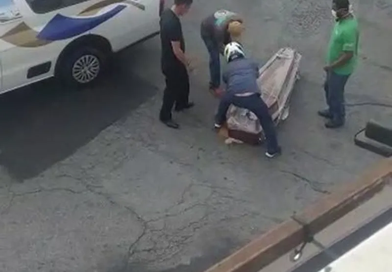 Homens tentam recolocar o caixão no veículo.