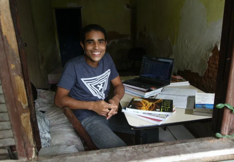 Pedro Carlos em casa, com os livros e notebook que ele usa nas primeiras aulas do curso